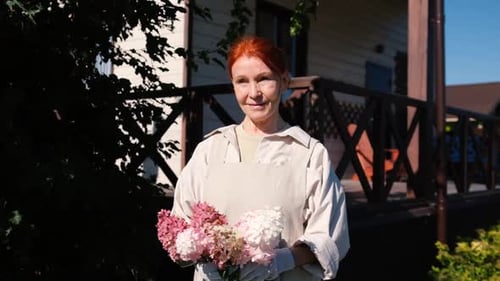 Old Retired Woman with Flowers From Her Garden in Her Hands Closeup Grandmother Looks at the Camera