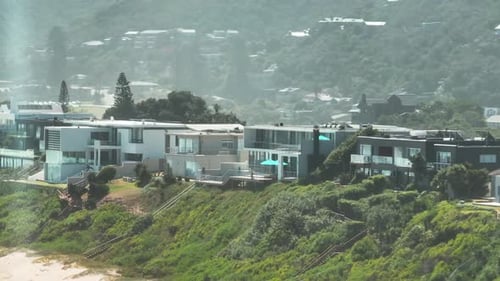 Slide and Pan Footage of Row of Houses Elevated Above Sand Beach Leading Along Sea Coast
