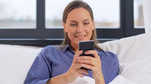 Woman using phone in bed smiling