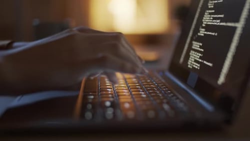 Hands Typing Code on Illuminated Laptop Keyboard