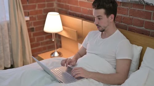 Man in Bed Cheering at Laptop Success