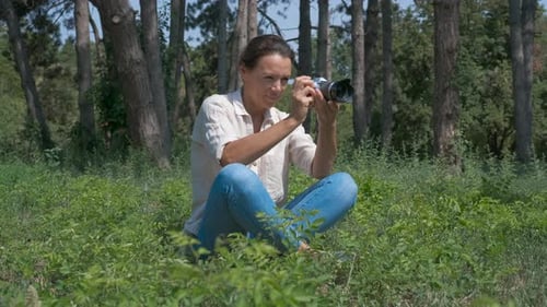 Woman Sits in Forest Taking Pictures with Camera