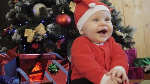 Child Near the Christmas Tree Laughs and Claps His Hands