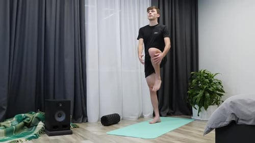 Athlete in black sports clothes stretches body before hard training in bright room. Yoga concept