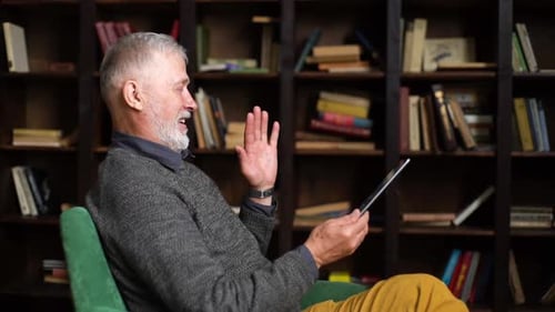 Side View of Happy Smiling Mature Adult Male Greeting and Waving Hand Talking By Digital Tablet