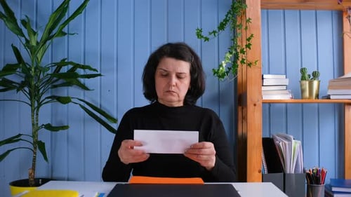 Woman Reading Letter with Worried Expression Indoors