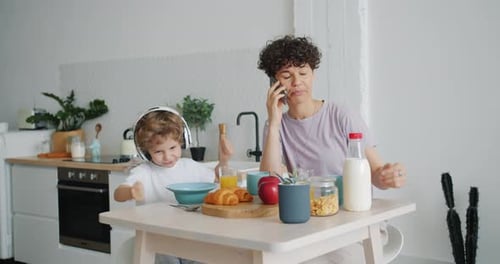 Boy Dances as Mom Talks on Phone at Breakfast