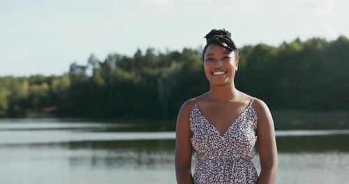 Beautiful Smiling Cheerful Woman in Floral Dress is Hanging Out at the Lake Her Hair is Tied Up in a
