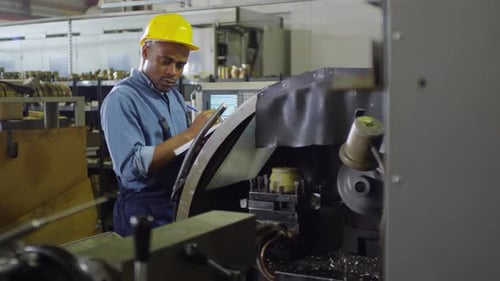 Factory Worker Inspecting Machinery with Clipboard and Pen