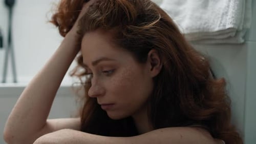 Sad Woman Sitting on Bathroom Floor with Head in Hands