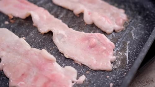 Cooking Pieces of Flavorful Sliced Organic Bacon Fried in Grill Pan