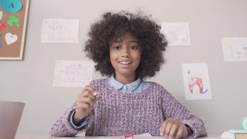 Smiling Girl Writing at School Desk Waving