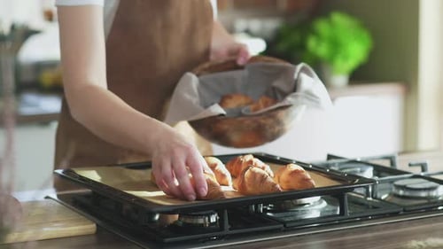 Woman Arranges Croissants on Baking Sheet in Kitchen