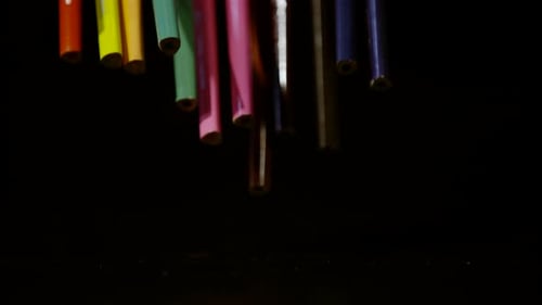 Colorful Pencils Drop in Slow Motion on Dark Surface
