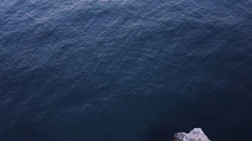 Top down tilt aerial view of waves splash against rocky seashore, background. Flight over high cliff