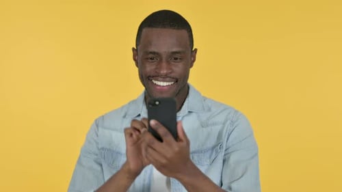 Man Smiling While Using Smartphone On Yellow Background
