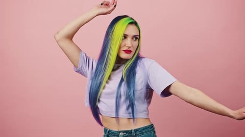 Young Woman with Rainbow Colored Hairstyle Dancing Over Pink Studio Background Enjoying Great Music