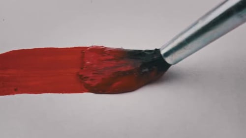Brush With Red Paint Draws a Line on White Paper in Macro
