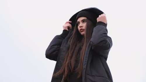 Fashion Portrait of Trendy Pretty Brunette Girl Putting on a Hood Outdoors. Female Model Wearing