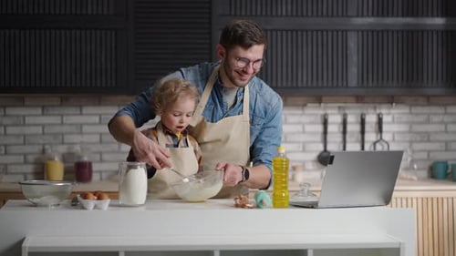 El joven padre y el hijo pequeño están cocinando por Vídeo tutorial Ver Vídeo en la computadora portátil y batir la masa