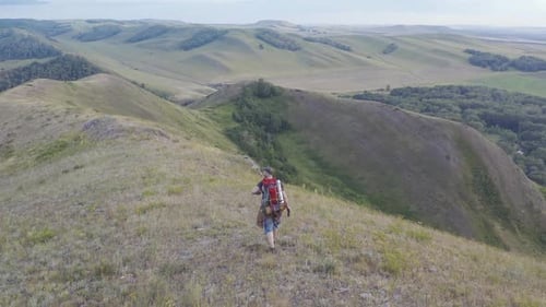 The Camera Follows a Hiker with a Backpack walking Along the Top of the Hill.