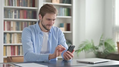Young Man Celebrates While Using Smartphone at Desk