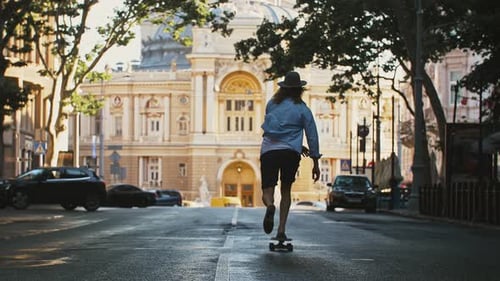 Young Male in Casual Outfit and Hat is Riding Skateboard Towards Yellow Truck Along Deserted City