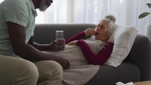 Man Giving Medication to Senior Woman on Sofa