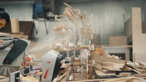Mann mit Brille und Kopfhörer beim Sägen von Holz mit Kreissäge in Holzwerkstatt