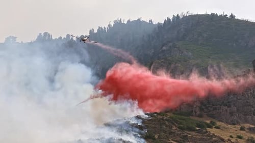 Airplane dropping fire retardant on wildfire burning on mountain