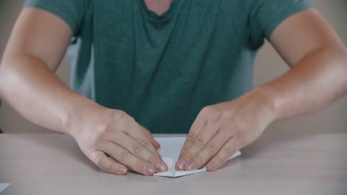 Man Folding White Paper at a Table