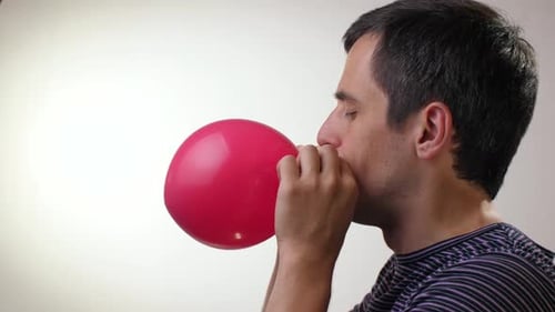 Man Blowing Up Red Balloon In Studio