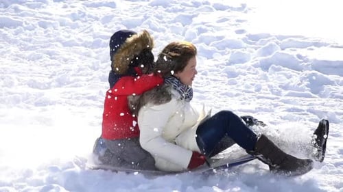 Asian Mother And Her Son Sliding On Sleds Down Snow Hill In Winter