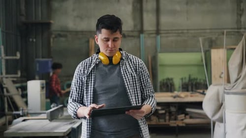 Business Owner Man Walking in Wood Workshop with Laptop Doing Inventory