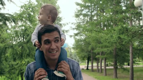 Father Carries Infant on Shoulders in Park