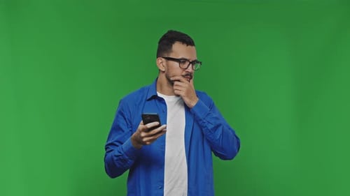 Attractive Guy Texting on His Phone Scratching His Beard Thinking Looking at Camera and on Green