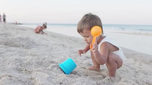 Boy Playing with Toys on the Beach Building Beads and Turrets Smiling at Someone Behind the Scenes