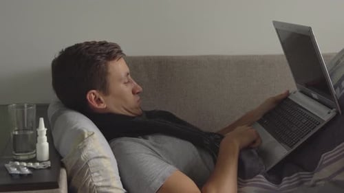 Man Lying on Couch with Cold Working on Laptop