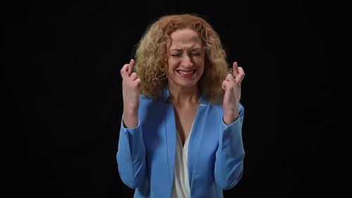 Woman Crossing Fingers in Hope Gesture Closing Eyes Praying at Black Background