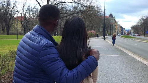 A Black Man and a Woman Stand in a Street with Their Backs To the Camera, Point at and Talk