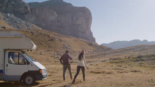 Man and Woman Walk Through Countryside with Mountains While Traveling By Camper Car Rbbro