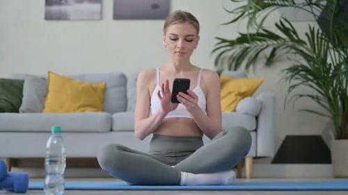 Woman Uses Smartphone on Exercise Mat at Home