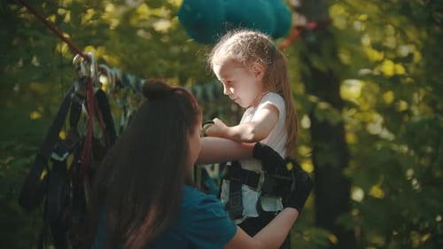 Une instructrice aide une petite fille à enfiler sa ceinture d'assurance pour l'aventure sur la corde