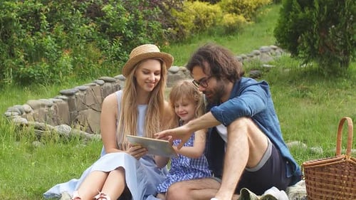 Beautiful Young Family Using Digital Tablet During Picnic at Countryside