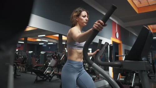 Young Woman Is Working Out on Stepper in a Gym. She Is Walking on Orbitrek for Cardio Intensity and