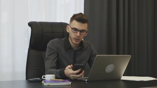 Businessman in suit and glasses talks on phone sitting in modern office. Business corporate concept