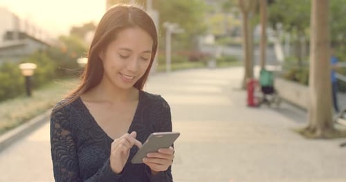 Woman Using Smartphone in Urban Park at Sunset