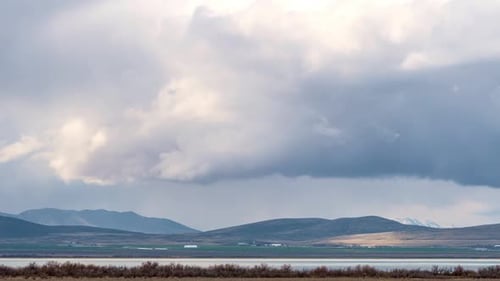 Storm clouds rolling over hills past lake