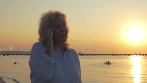 Senior Woman Having Phone Talk on Beach at Sunset