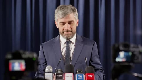Man Giving Speech at Press Conference with Microphones